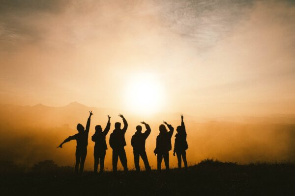 Silhouette einer Gruppe von Menschen vor einem Sonnenuntergang, die freudig die Arme heben.