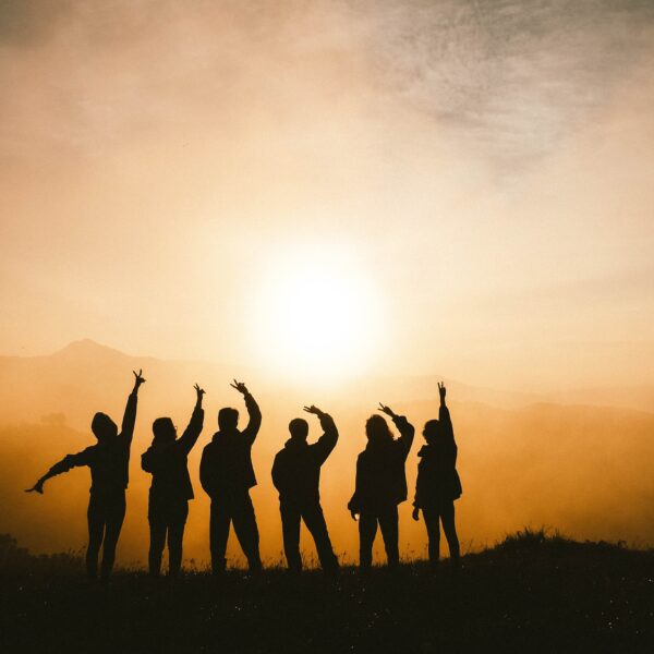 Silhouette einer Gruppe von Menschen vor einem Sonnenuntergang, die freudig die Arme heben.